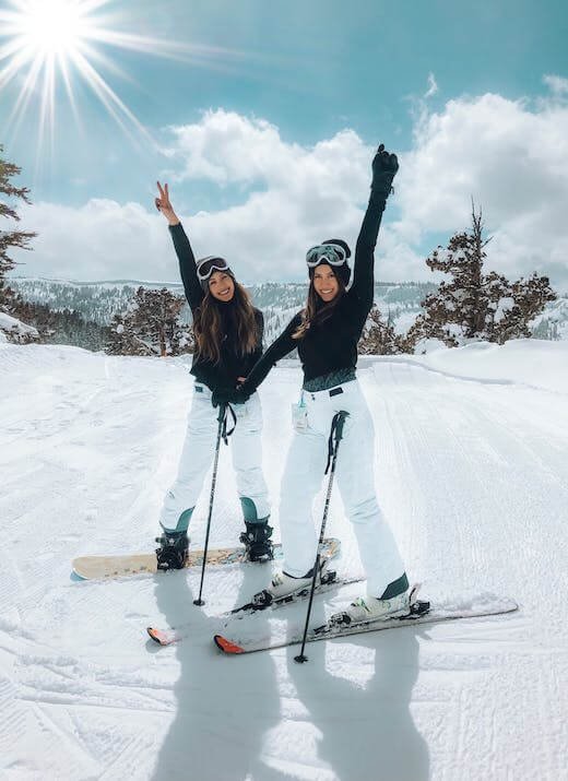 Two girls wearing skis and smiling on the slopes