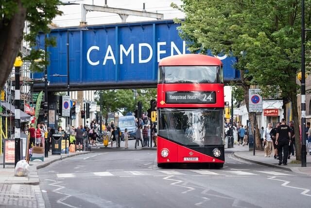 Red double decker bus drives through Camden, London