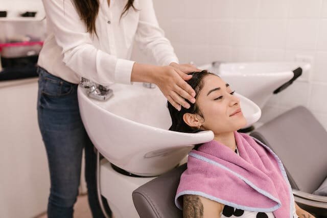 A woman getting a scalp massage by a hair stylist.