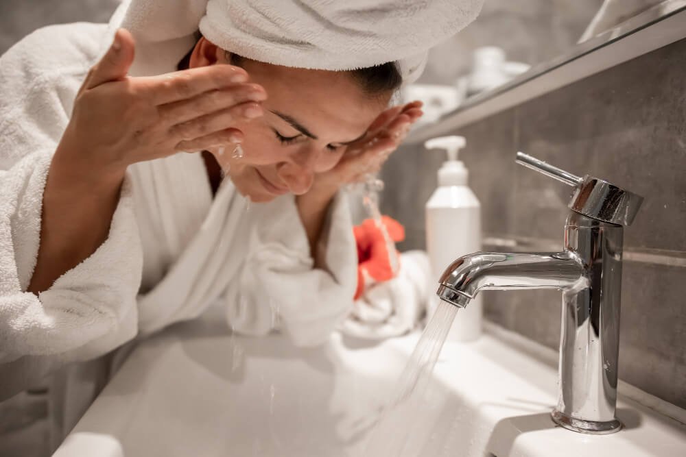 A woman washes her face in the bathroom sink. Should you wash your face before working out?