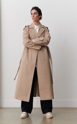 A woman wears a long camel trench coat