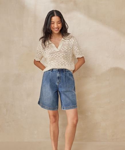A model wears a long denim shorts with a cream crochet top