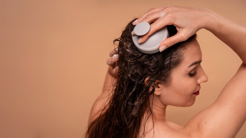 A woman is doing a scalp massage on wet hair with a shampoo brush