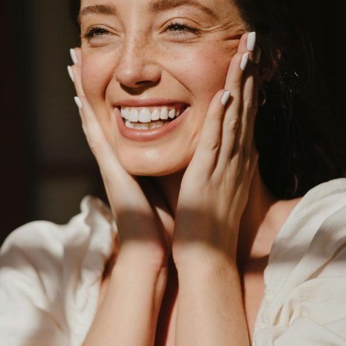A woman with clear skin holds her face in her hands