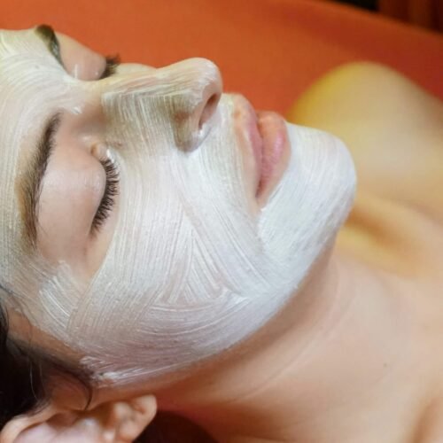 A woman is having a facial mask applied to her face.