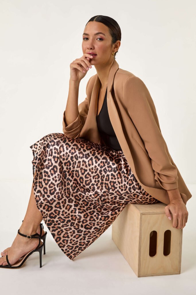 9 leopard skirt outfit ideas: A model wears a midi satin leopard print skirt, a tan blazer and strappy heeels.