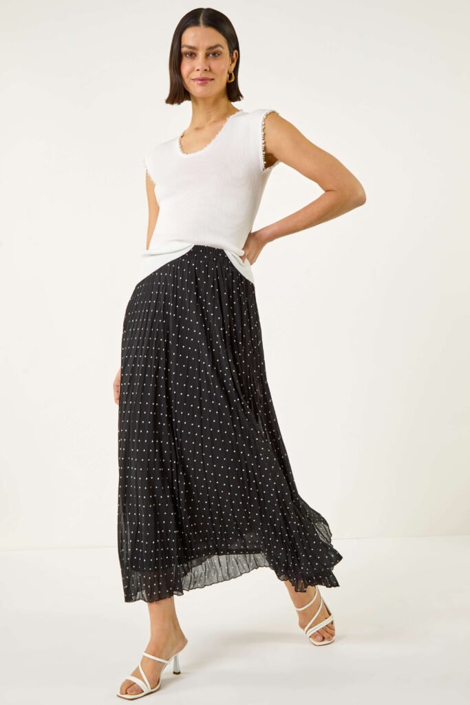 5 Easy Casual Dinner Outfits To Get Ready In Minutes
A woamn with short brown hair wears a white short-sleeved top, a balc and white polka dotted maxi skirt and white strappy sandals.