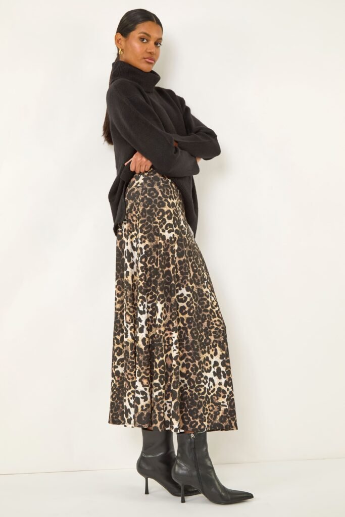 A model wears a midi leopard print skirt, a black roll neck jumper, and black knee high boots. 