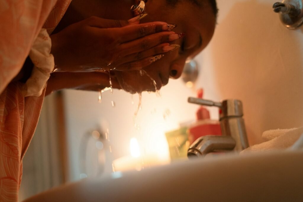A woman with long nails is washing her face in the sink