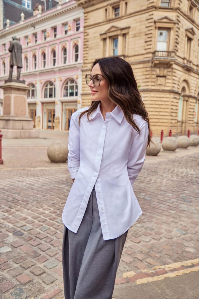Michelle Keegan wears a long sleeve white shirt, tailored grey trousers and aviator sunglasses.
