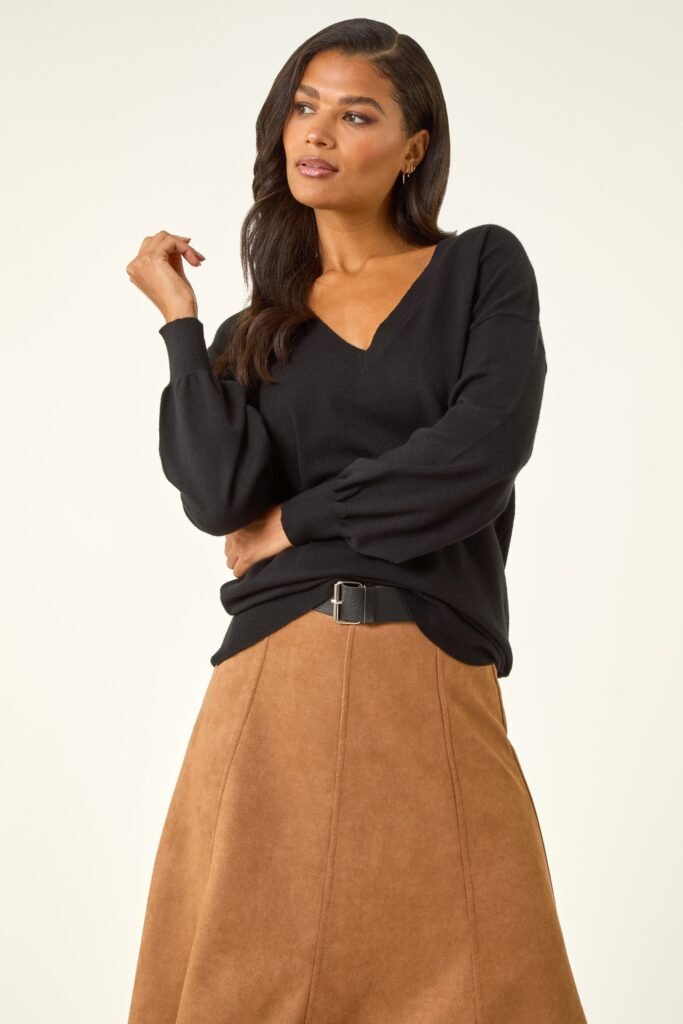 A model with long brown hair wears a black V-Neck jumper, a suede brown skirt with a black belt.